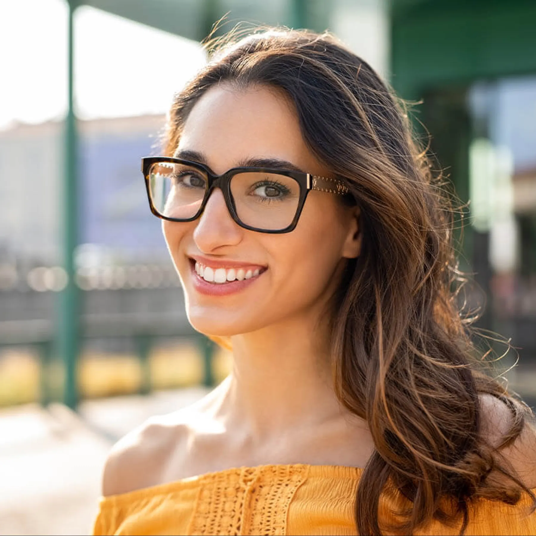 Smiling woman wearing glasses in a sunny outdoor setting, showcasing bright colors and casual style.