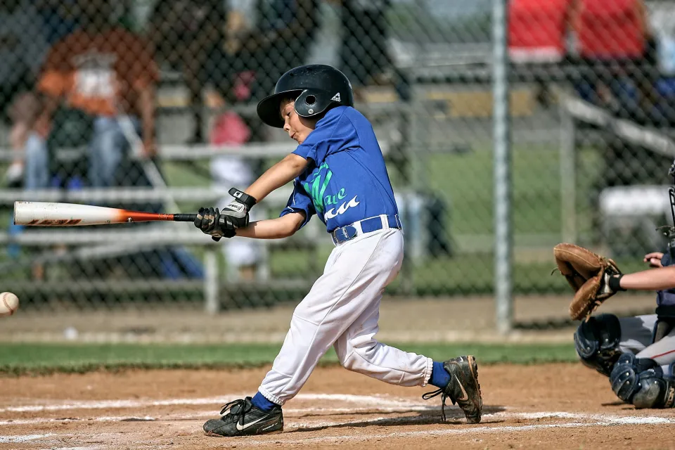 Young boy in blue jersey swinging baseball bat during a youth baseball game at home plate.